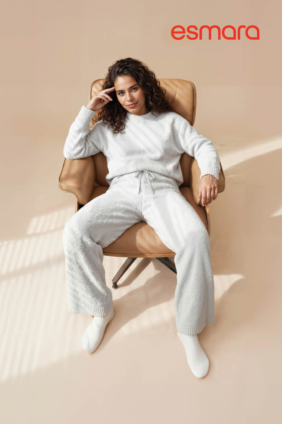 Femme en ensemble de détente blanc assise dans un fauteuil en cuir.