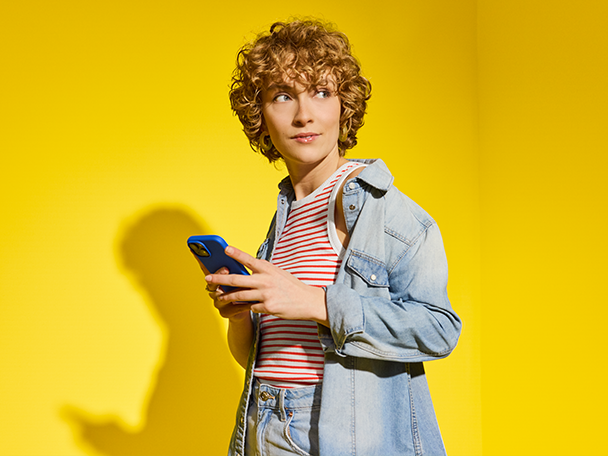 Femme utilisant un smartphone avec coque bleue, sur fond jaune.