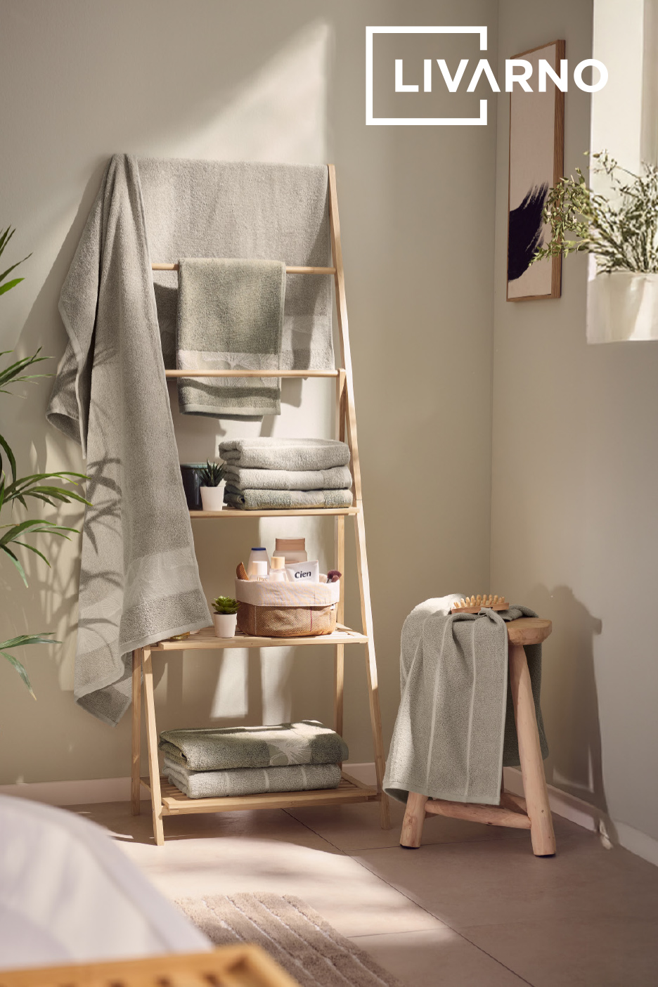 Serviettes de bain vertes et grises sur une étagère en bois et un tabouret dans une salle de bain lumineuse.