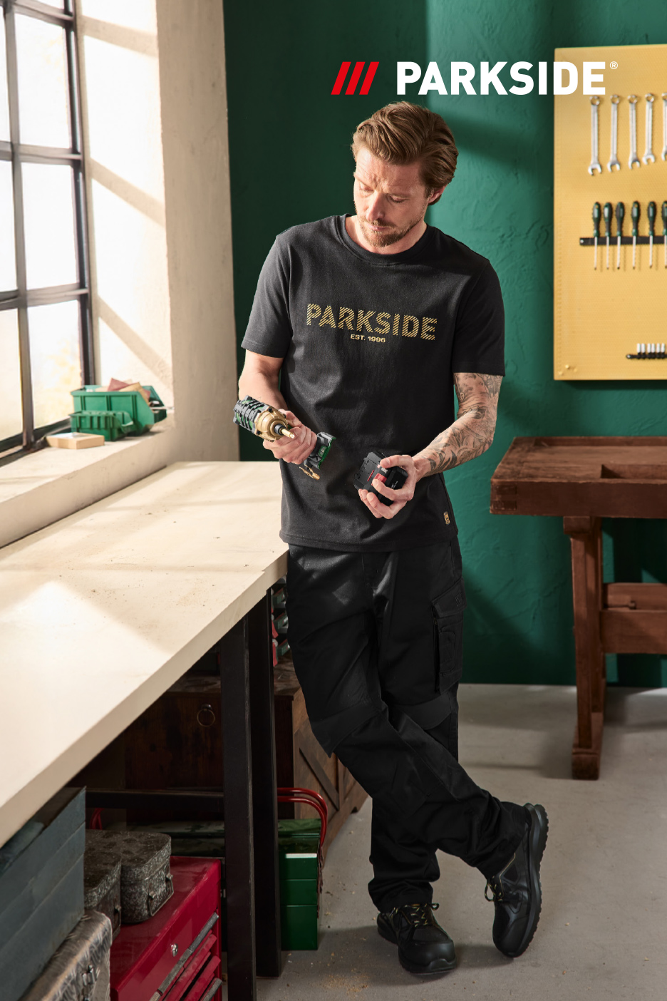 Un homme dans un atelier, tenant une perceuse sans fil et une batterie.