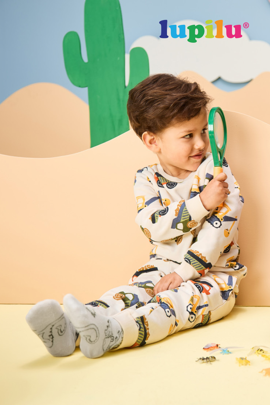 Enfant en pyjama à motifs de véhicules, explorant avec une loupe dans un décor de désert.