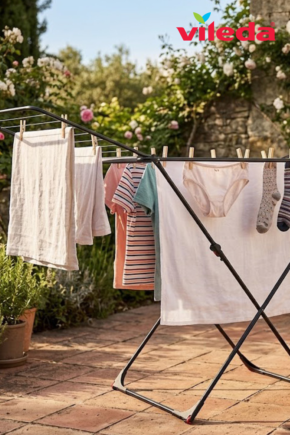 Un étendoir à linge noir avec des vêtements séchant au soleil dans un jardin fleuri.