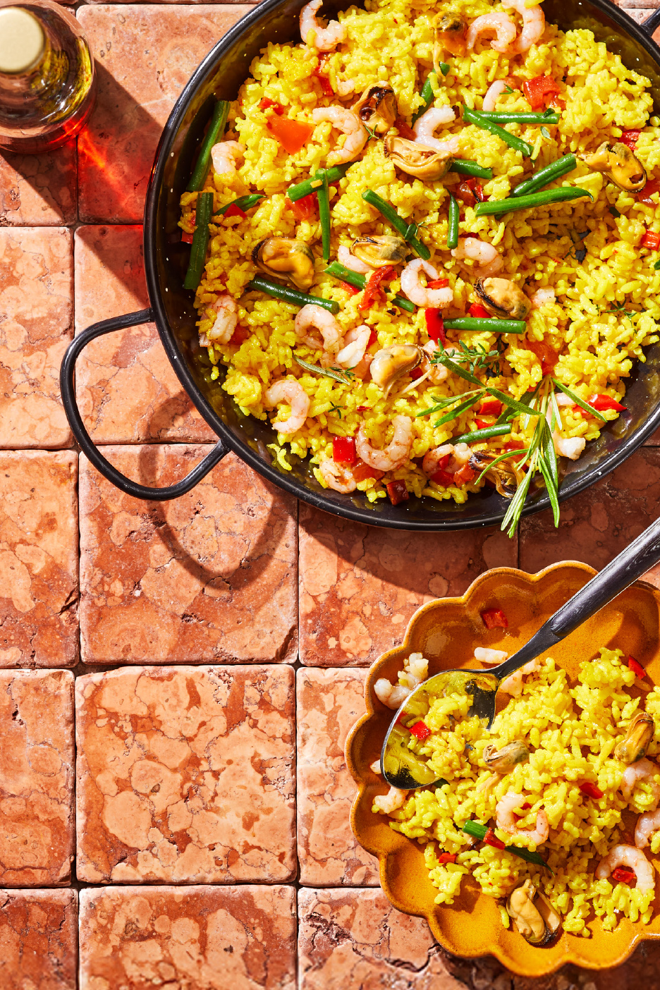 Paella aux fruits de mer et légumes dans une poêle et une assiette sur des carreaux de terre cuite.