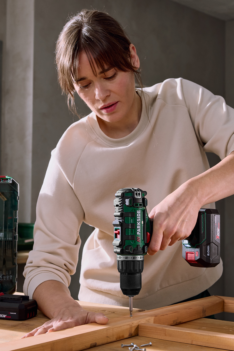 Une femme utilise une perceuse-visseuse sans fil pour visser une vis dans une pièce de bois.