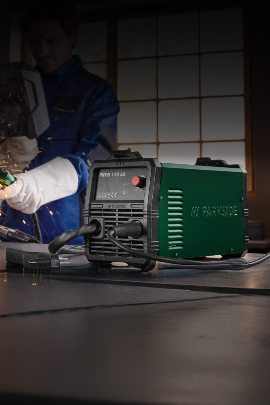 Un soudeur utilise un poste à souder vert et noir, des étincelles volent.