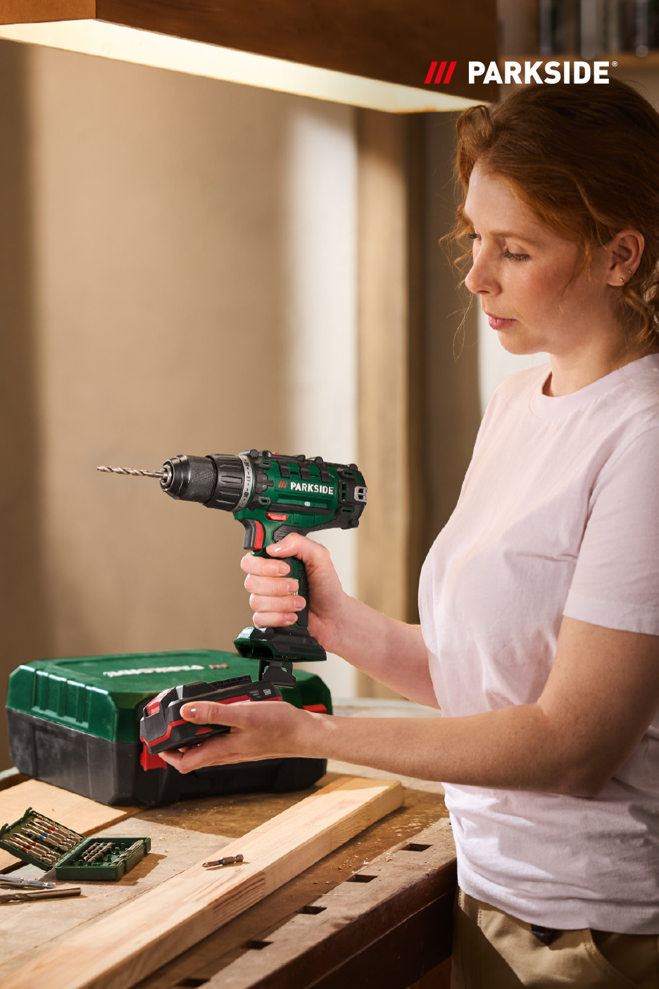 Une femme tient une perceuse sans fil avec une batterie, prête à l'emploi sur un établi.