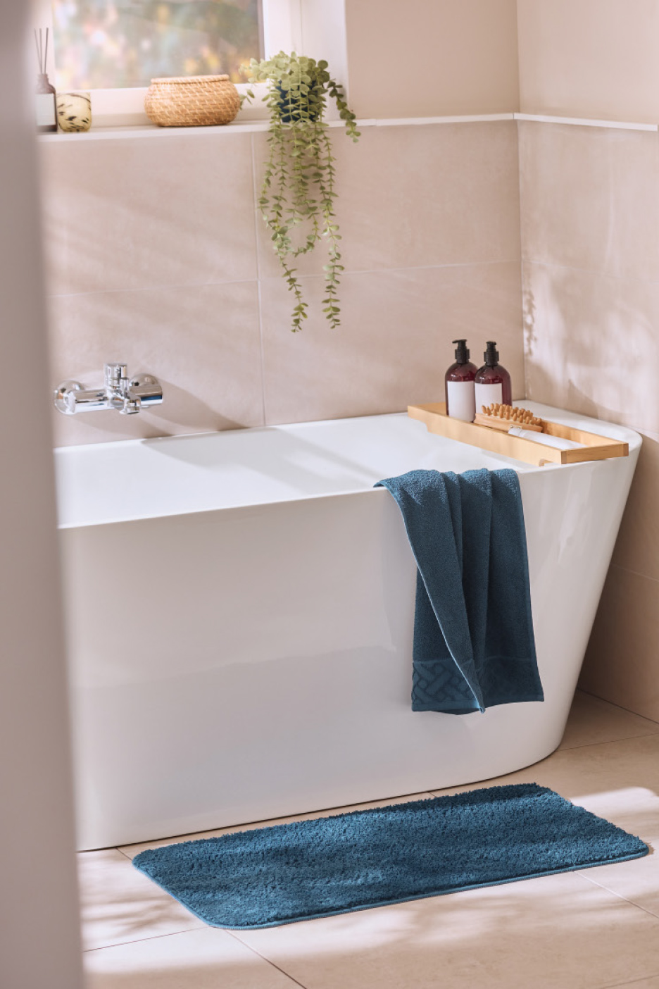 Baignoire blanche avec serviette et tapis de bain bleus, et plantes décoratives.