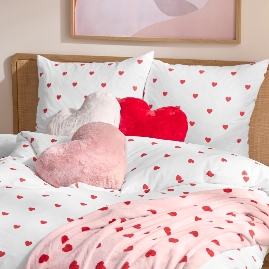 Literie blanche à cœurs rouges avec coussins en forme de cœur et couverture rose.