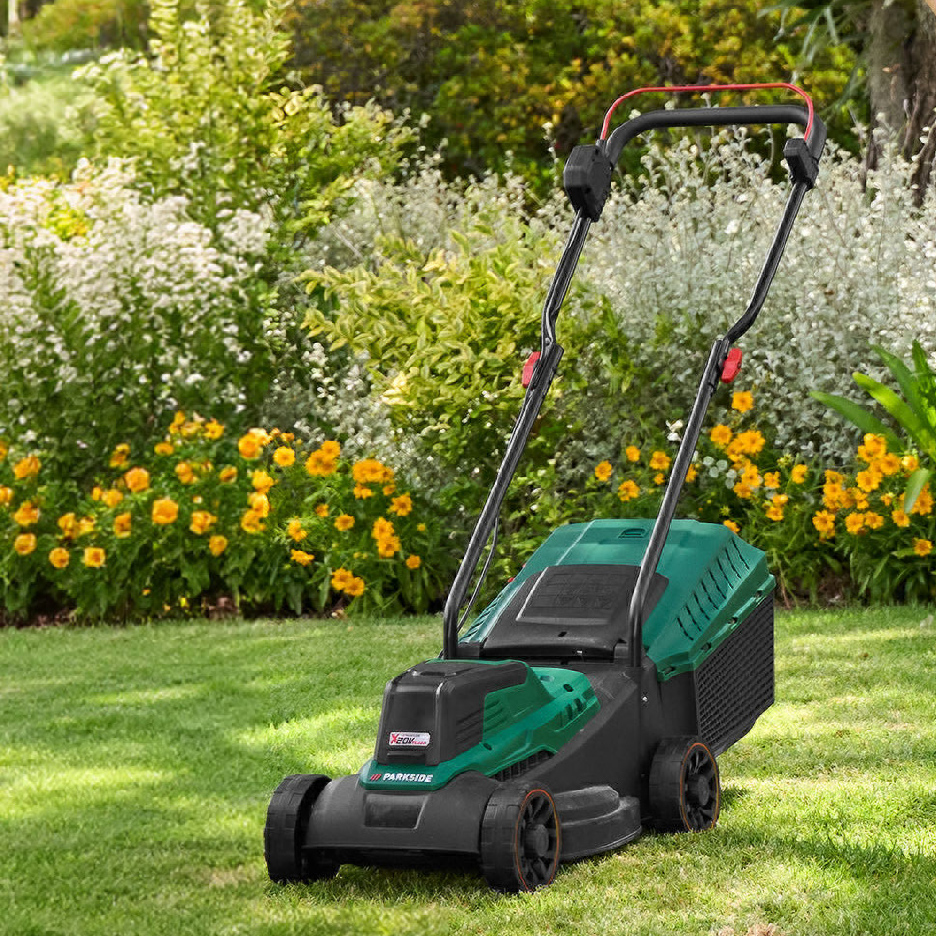 Tondeuse à gazon sans fil verte et noire sur une pelouse, avec des fleurs en arrière-plan.