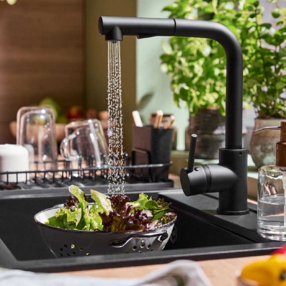 Robinet de cuisine noir avec douchette extractible, lavant de la salade dans un évier.